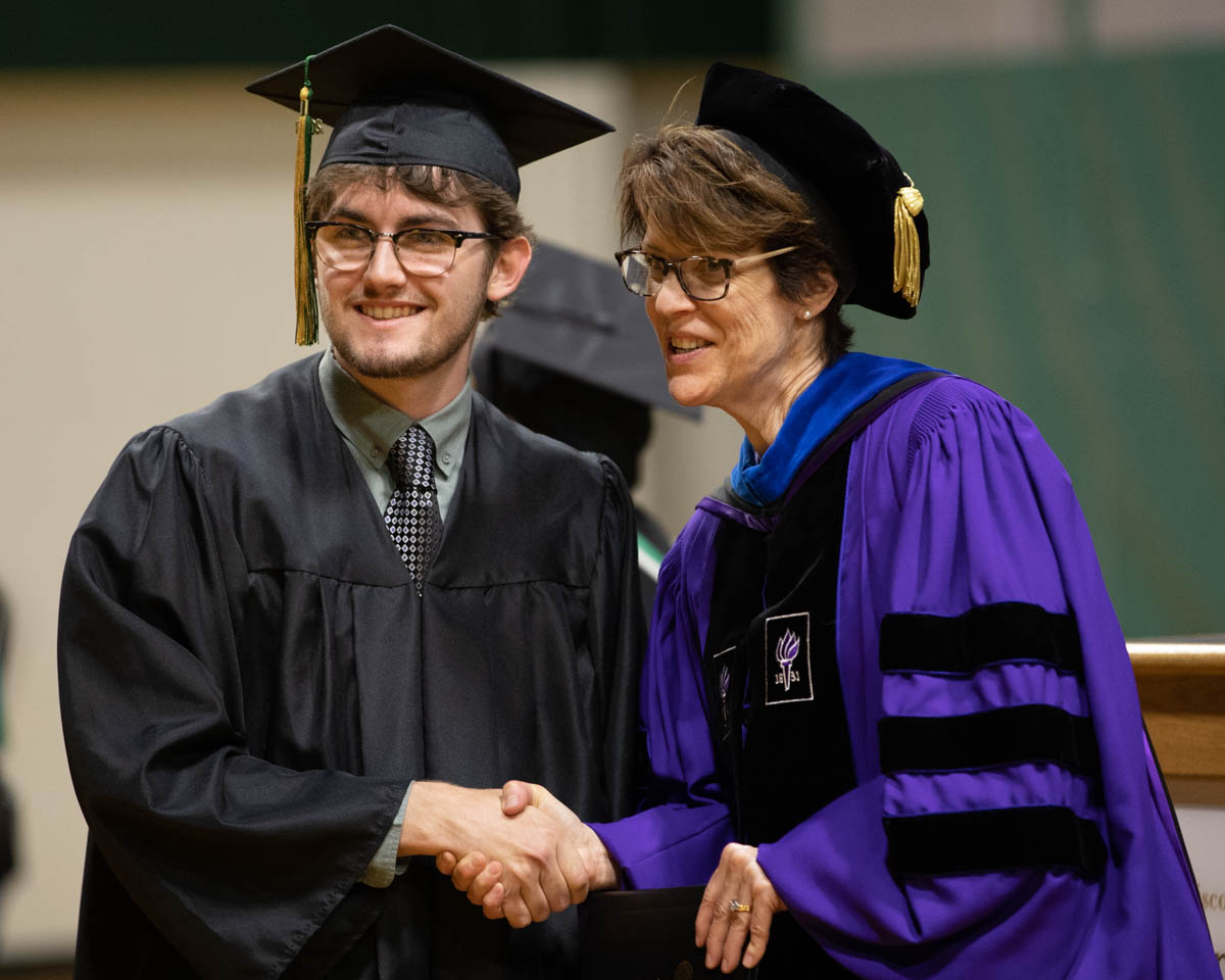College President at graduation shaking hand of male graduate
